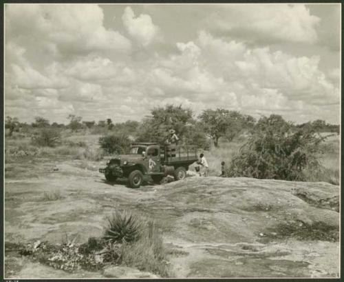 Power Wagon at a waterhole; three people filling barrels with buckets of water