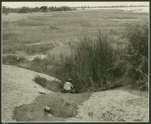 Expedition member crouching by a waterhole; Gautscha Pan in the background