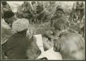 Lorna Marshall and Frederick !Gaeb taking notes, seen from behind; unidentified Ju/'hoansi in front of them