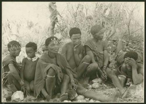 Ju/'hoan women and children sitting; man standing in the background