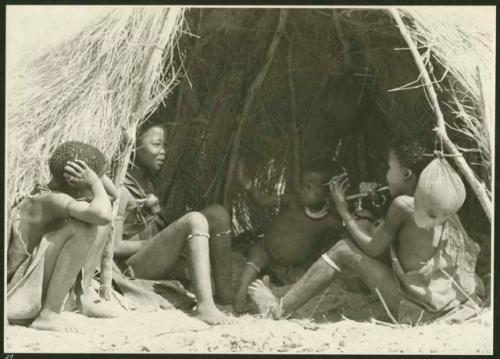 Ju/'hoan children sitting inside a skerm; water bag made from animal stomach hangs from the side of the entrance