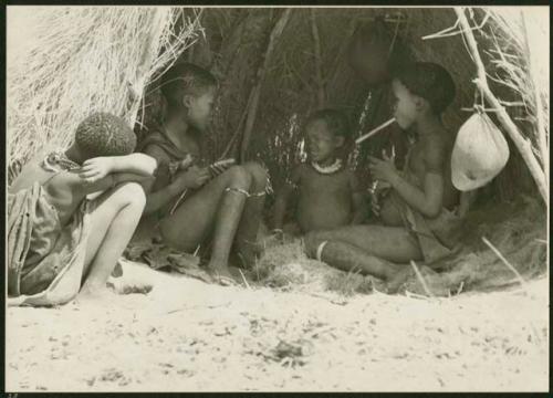 Ju/'hoan children sitting inside a skerm; water bag made from animal stomach hangs from the side of the entrance