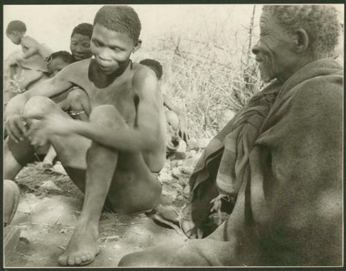 Elderly man and young man sitting; other people in the background