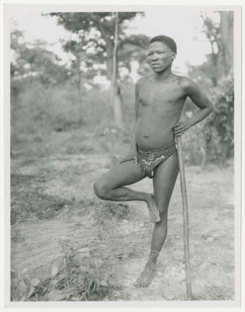 Man standing on one leg leaning against his stick (print is flipped)