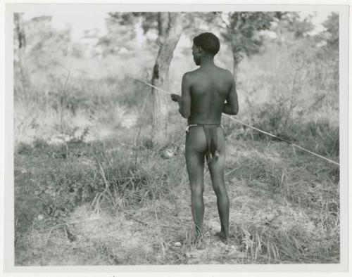 Man holding a spring-hare prodder, seen from behind (print is a cropped image)