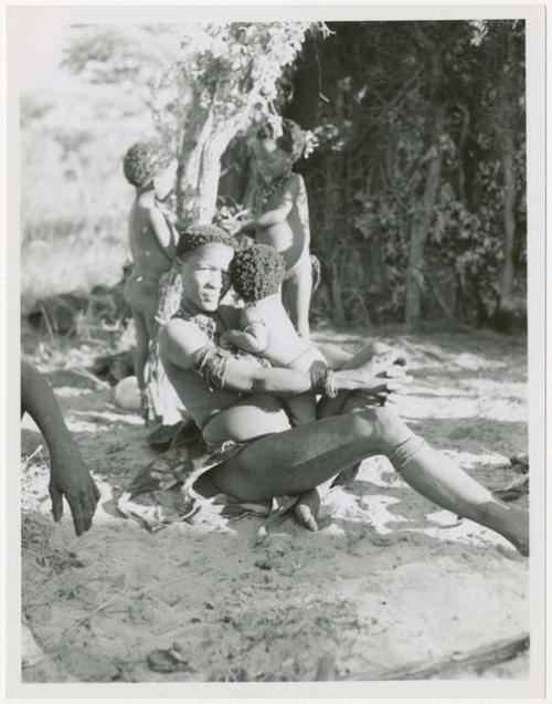 Woman seated with a child; two children in the background