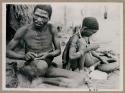 "Gao Medicine" binding an arrow shaft with sinew, with Di!ai sitting next to him pounding something with a stone