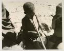 Two children sitting with a tsama melon; one child sucking end of a digging stick