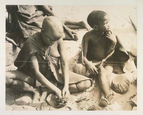 Girl pounding tsama melons seeds in a piece of gourd used as a receptacle
