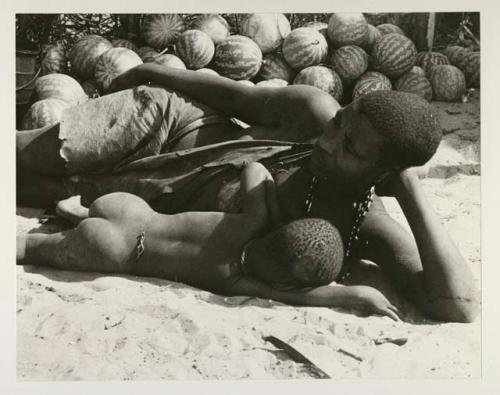 Mogatsiposi lying on her side nursing child, in front of pile of tsama melons
