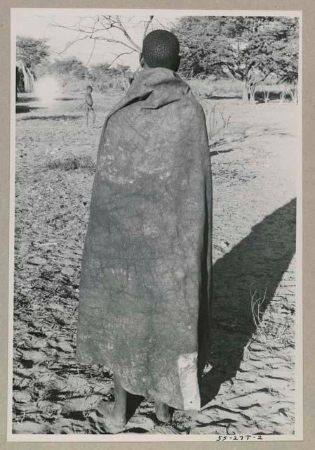 Woman standing wearing a kaross, seen from behind
