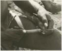 !Gai sharpening edge of his scraping tool against the metal point of his drill (print is a cropped image)