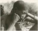 /Twikwe sitting with hands against cheek, close-up (print is a cropped image)