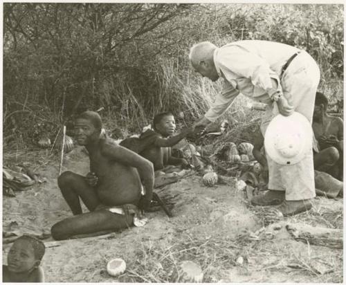 Laurence Marshall shaking hands with Tsekue, !Gai sitting beside Tsekue (print is a cropped image)