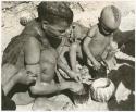 Tsekue and N!whakwe with tsama melon seeds in tins, used as containers (print is a cropped image)