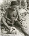 Oukwane holding cord in his toes, smoothing cord with grass (print is a cropped image)