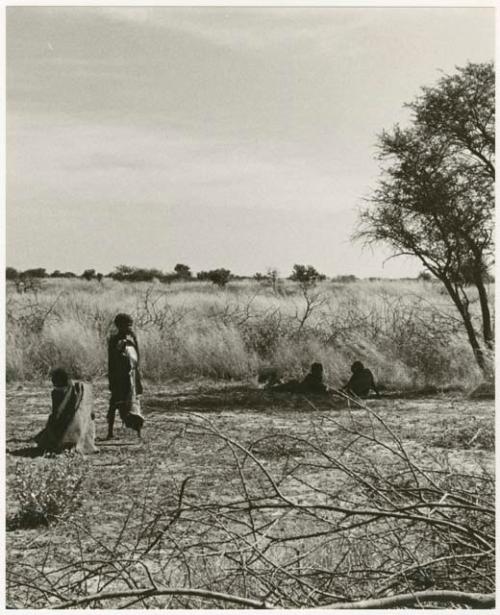 /Twikwe clearing ground with digging stick, someone standing next to her; children lying in shade (print is a cropped image)