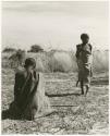 /Twikwe clearing ground with digging stick, someone standing nearby; two children lying in the shade (print is a cropped image)