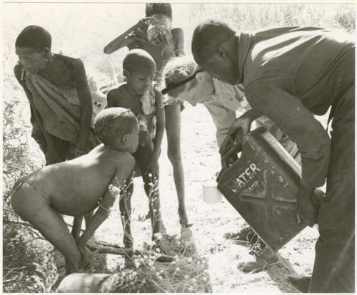 Simon Molamo and Lorna Marshall pouring water into a cup for three boys beside them; boy drinking from a can (print is a cropped image)