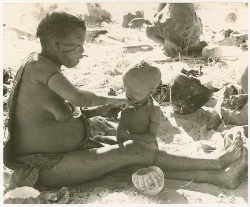 Tsekue giving N!whakwe a piece of meat, cutting it off at his lips with a knife (print is a cropped image)