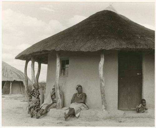 Three women and a child sitting against the outside of a house (print is a cropped image)