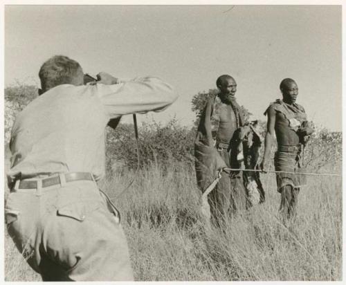 Blind man being led by another man, Daniel Blitz photographing (print is a cropped image)