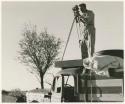 Daniel Blitz with movie camera on top of expedition truck (print is a cropped image)