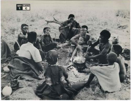 [No folder title]: //Kushay, "Little ≠Gao", !Ungka, and other unidentified people seated around a pot on a fire while "Old Gau" stirs the pot (print is a cropped image)