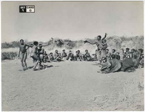 [No folder title]: Two women and boys dancing, and a group of women sitting and clapping (print is a cropped image)