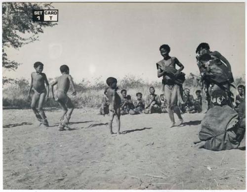 [No folder title]: /Naoka and boys dancing, with a group of women sitting and clapping in the background (print is a cropped image)