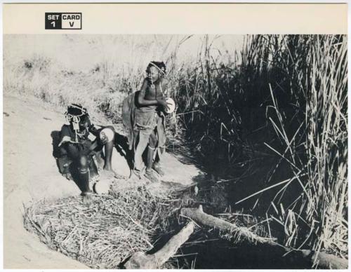 [No folder title]: Bau (daughter of Ti!kay) filling an ostrich eggshell with a tortoise shell dipper, with another woman sitting next to her