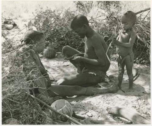 !Gai, Tsekue, and N!whakwe sitting at their place in the werft (print is a cropped image)