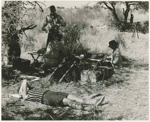 Expedition members setting up sound equipment, with a person standing next to a tree in the background (print is a cropped image)