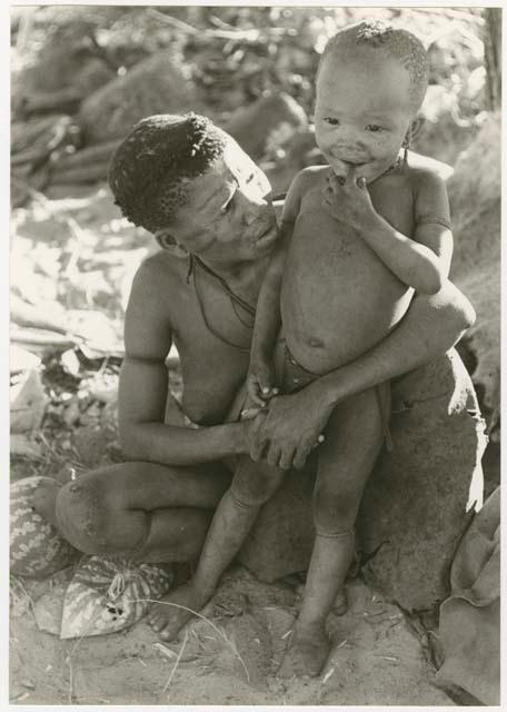 Tsekue sitting and holding N!whakwe against her knee (print is a cropped image)