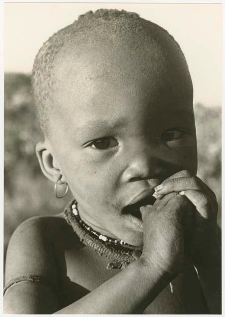 N!whakwe with hands in his mouth, close-up (print is a cropped image)