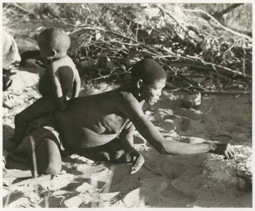 /Twikwe getting a coal to light her pipe, N!whakwe sitting on her back (print is a cropped image)