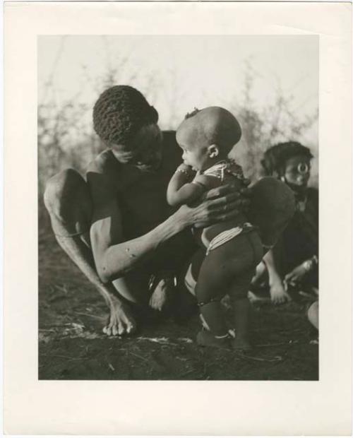 "Gao Medicine extended family, Band 1": "Gao Medicine" squatting and holding Norna (print is a cropped image)