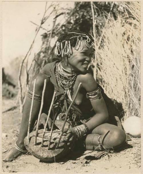 "Band 5, Khuan//a the Musician (85)": Khuan//a sitting in front of a skerm and playing the //guashi (print is a cropped image)