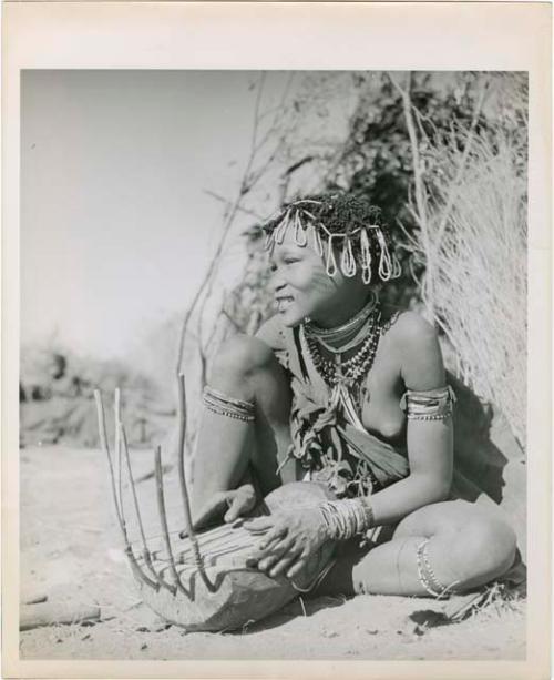 "Band 5, Khuan//a the Musician (85)": Khuan//a sitting in front of a skerm and playing the //guashi (print is a cropped image)