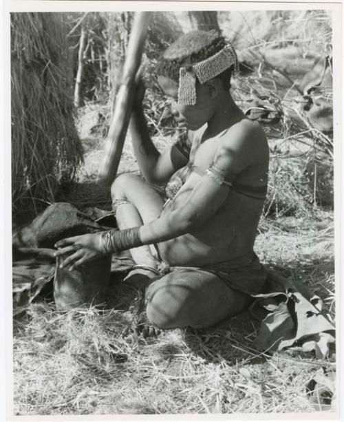 [No folder title]: //Kushay ("Gao Helmet's" second wife) pounding with mortar and pestle, wearing ornaments and ostrich eggshell beads on her head (print is a cropped image)