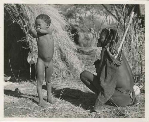 [No folder title]: /Ti!kay sitting in front of a skerm and holding his hunting equipment, with a boy standing next to him (print is a cropped image)