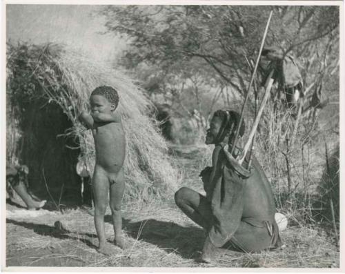 [No folder title]: /Ti!kay sitting in front of a skerm and holding his hunting equipment, with a boy standing next to him (print is a cropped image)