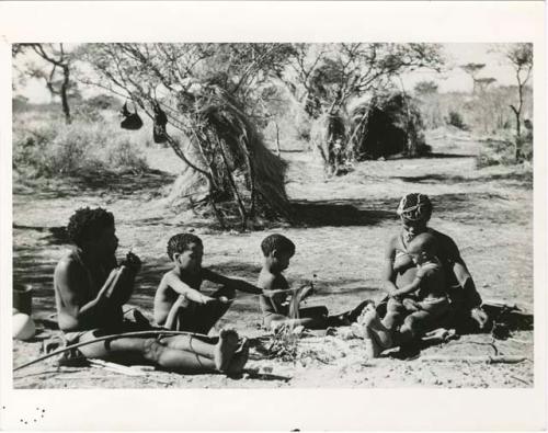 ≠Toma working on arrows and sitting with his family, including Tsamgao, /Gaishay and !U, who is holding Norna on her lap (print is a cropped image)