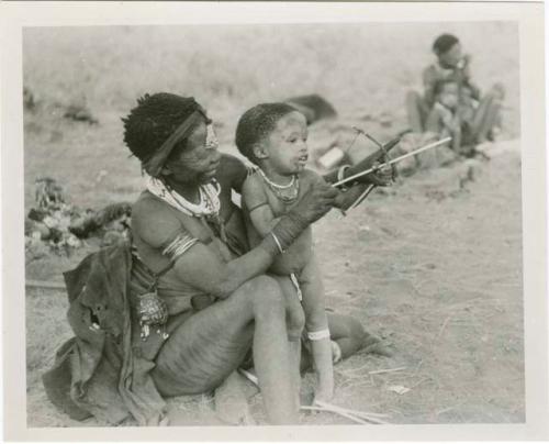 [No folder title]: Di!ai showing her son, Debe, how to hold a toy bow and arrows (print is a cropped image)