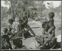 "Group of Band 2  Khuan//a #52  //Kushay II #32": Group of Ju/'hoansi seated including Khuan//a (Gau's second wife) and //Kushay ("Gao Helmet's" second wife) sitting and playing the //guashi with her child seated on her shoulder (print is a cropped image)