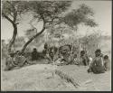 "Band 2, Gao Helmet #28 & extended family": "Gao Helmet" making an assegai head in his werft, with members of his band sitting around him (print is a cropped image)