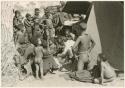 "Band 2, Old /Gasa 61": Group of Ju/'hoansi, Kernel Ledimo, Lorna Marshall gathered around to look at beads, seemingly in the cold (print is a cropped image)