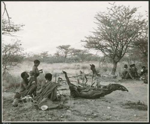 Band 1, an overnight encampment: ≠Toma sitting and kissing Norna, with !U sitting next to him, and other people in the background (print is a cropped image)