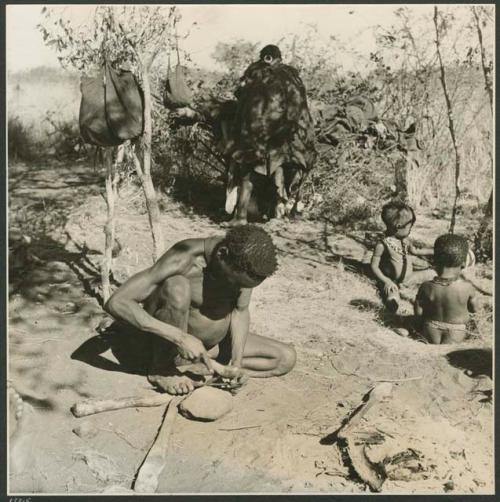 "Gao Helmet and family, Band 2": "Gao Helmet" hammering and shaping an assegai blade with a piece of metal, and //Kushay, his second wife, standing near him