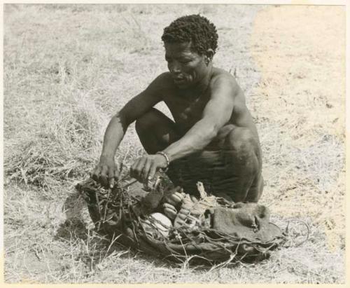 "≠Toma, Envelope 2 (of 4)": ≠Toma lining a carrying net with a small kaross to pack it with rattles, ostrich eggshells, etc. (print is a cropped image)